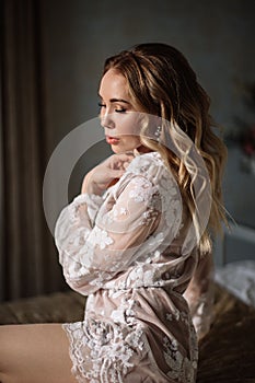 Bride`s morning. Fine art wedding. Portrait of a young bride in white lace boudoir with wavy blonde hair and a bouquet