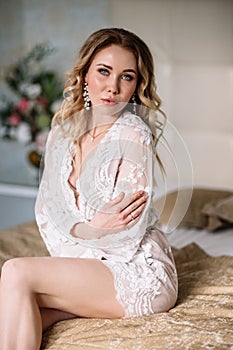 Bride`s morning. Fine art wedding. Portrait of a young bride in white lace boudoir with wavy blonde hair and a bouquet