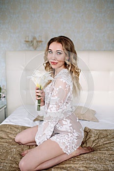 Bride`s morning. Fine art wedding. Portrait of a young bride in white lace boudoir with wavy blonde hair and a bouquet