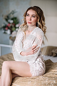 Bride`s morning. Fine art wedding. Portrait of a young bride in white lace boudoir with wavy blonde hair and a bouquet