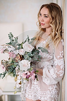 Bride`s morning. Fine art wedding. Portrait of a young bride in white lace boudoir with wavy blonde hair and a bouquet