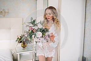 Bride`s morning. Fine art wedding. Portrait of a young bride in white lace boudoir with wavy blonde hair and a bouquet