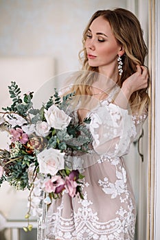 Bride`s morning. Fine art wedding. Portrait of a young bride in white lace boudoir with wavy blonde hair and a bouquet