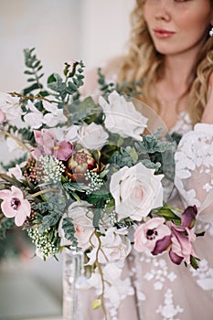 Bride`s morning. Fine art wedding. Portrait of a young bride in white lace boudoir with wavy blonde hair and a bouquet