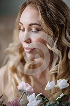 Bride`s morning. Fine art wedding. Portrait of a young bride in white lace boudoir with wavy blonde hair and a bouquet