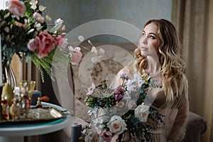 Bride`s morning. Fine art wedding. Portrait of a young bride in white lace boudoir with wavy blonde hair and a bouquet