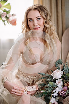 Bride`s morning. Fine art wedding. Portrait of a young bride in white lace boudoir with wavy blonde hair and a bouquet