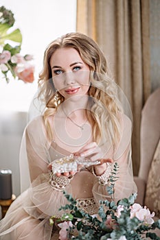 Bride`s morning. Fine art wedding. Portrait of a young bride in white lace boudoir with wavy blonde hair and a bouquet