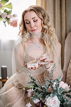 Bride`s morning. Fine art wedding. Portrait of a young bride in white lace boudoir with wavy blonde hair and a bouquet