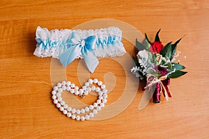 Bride's wedding accessories, white garter with blue ribbon, bracelet of pearls and cute little boutonniere. Preparing