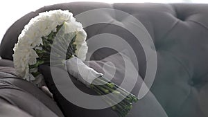 The bride's wedding bouquet is lying on the sofa in daylight.