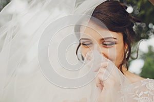 Bride shines standing with closed eyes and hiding her smile behind a veil