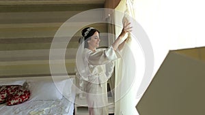 Bride in silk dressing gown holding and admiring her beautiful wedding dress.