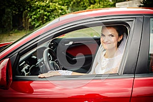 The bride sits behind the stering wheel of a red sports car photo