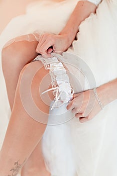 Bride is sitting on the bed and trying the garter
