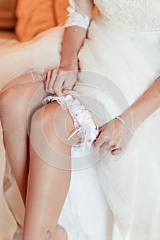 Bride is sitting on the bed and trying the garter