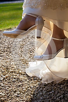 A bride sitting on a chair outside, at the bride`s feet there are designer high-heeled shoes