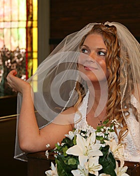 Bride sitting in a church pew holding her veil photo