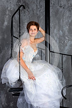 Bride sitting on spiral staircase in loft apartment. Woman dressed in wedding dress with lace, copy space for text