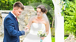 Bride slipping ring on finger of groom at wedding