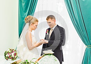 Bride slipping ring on finger of groom at wedding