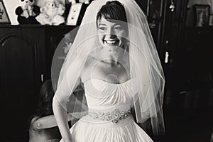 Bride smiles sincerely while bridesmaid buttons up her dress