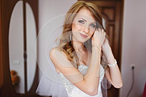 Bride smiles tender while putting on jewerly