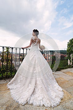 The bride is standing on  Balkon, dress with a big train, looks at the city of Prague