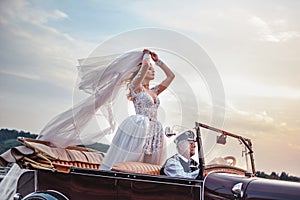 Bride standing in classic convertible while being driven