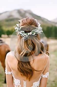 Bride is standing with her back in a beautiful lace dress. Bride& x27;s head is adorned with a wreath of green olive branches