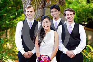 Bride standing with her three groomsmen outdoors under large tre photo