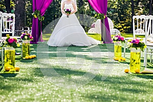 Bride standing in wedding archway with chairs on on each side