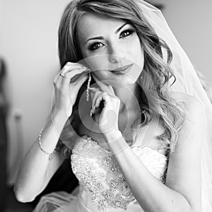 Bride with stunning make-up adjusts her jewerly in a room