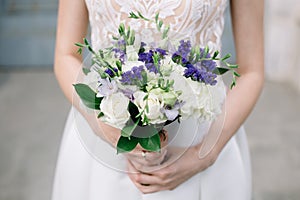 Bride in a stylish delicate white dress on the wedding day keeps a bouquet of light purple flowers. Wedding festive