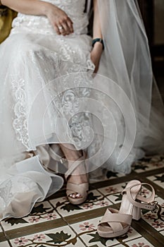 A bride is taking off her shoes. She is wearing the white wedding dress