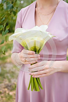 Bride in tender pink wedding dress holding white calla lilies bouquet. Minimalists style dressing, nude manicure. Closeup vertical