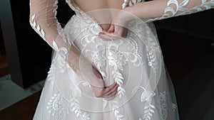 Bride ties and put on the wedding dress. Morning preparation of the bride with white gown. Zip up