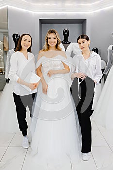 The bride-to-be chooses a dress for the wedding. A dressmaker\'s assistant is fitting a dress for the bride