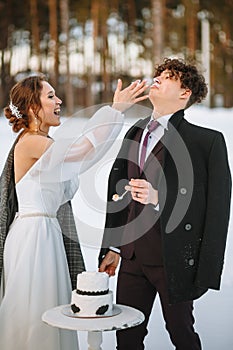 The bride wants to smear the groom`s face with a piece of wedding cake. Shooting in the winter forest