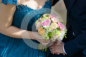 Bride wearing a blue dress and groom at the wedding with focus on bride`s hands holding a large round bouquet