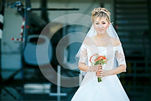 Bride with wedding bouquet on background of helicopter in hangar