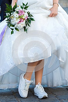 Bride with a wedding bouquet dressed in white dress showing sneakers on her legs