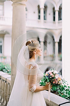 Bride with the wedding bouquet is spending time on the old balcony.