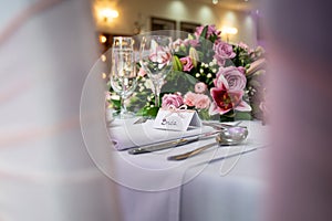 Bride wedding breakfast place setting with name card on top table waiting for arrival groom and pink roses and shiny glasses