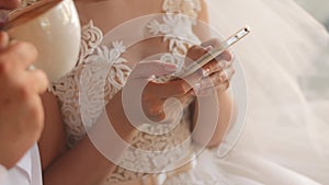 Bride in wedding dress holding smartphone in hands. Groom is drinking cappuccino.