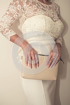 Bride in a wedding dress holds in hand a white bag. Beautiful manicure. Wedding day. Wedding rings.