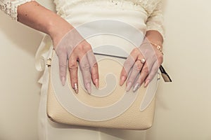 The bride in a wedding dress holds in hand a white bag. Beautiful manicure. Wedding day. Wedding rings.
