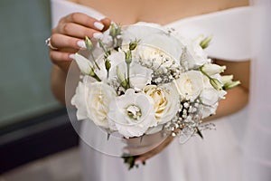 The bride in a wedding dress and a long veil holds a white wedding bouquet of roses