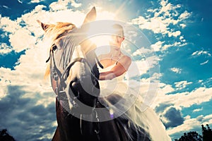 Bride in wedding dress riding a horse, backlit