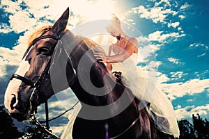 Bride in wedding dress riding a horse, backlit